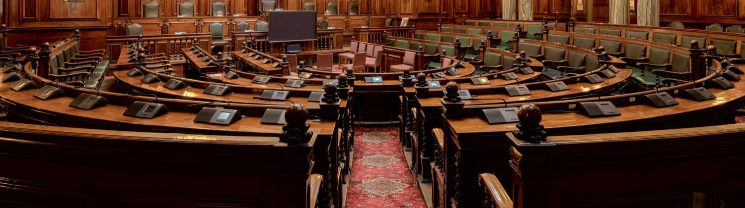 Empty city council chamber with wood-paneled walls and rows of seats